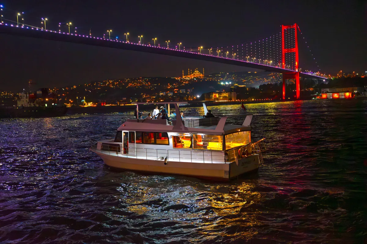 Motor yacht with a group on deck under the illuminated Bosphorus Bridge at night